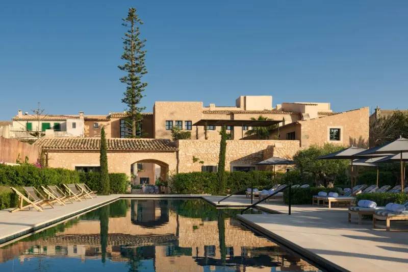 Piscina de Can Ferrereta, con tumbonas, el pino de Norfolk y las casas de piedra del hotel al fondo